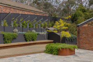 Contemporary timber deck with charcoal steel retaining walls built-in seating and layered native plantings Ivanhoe Melbourne