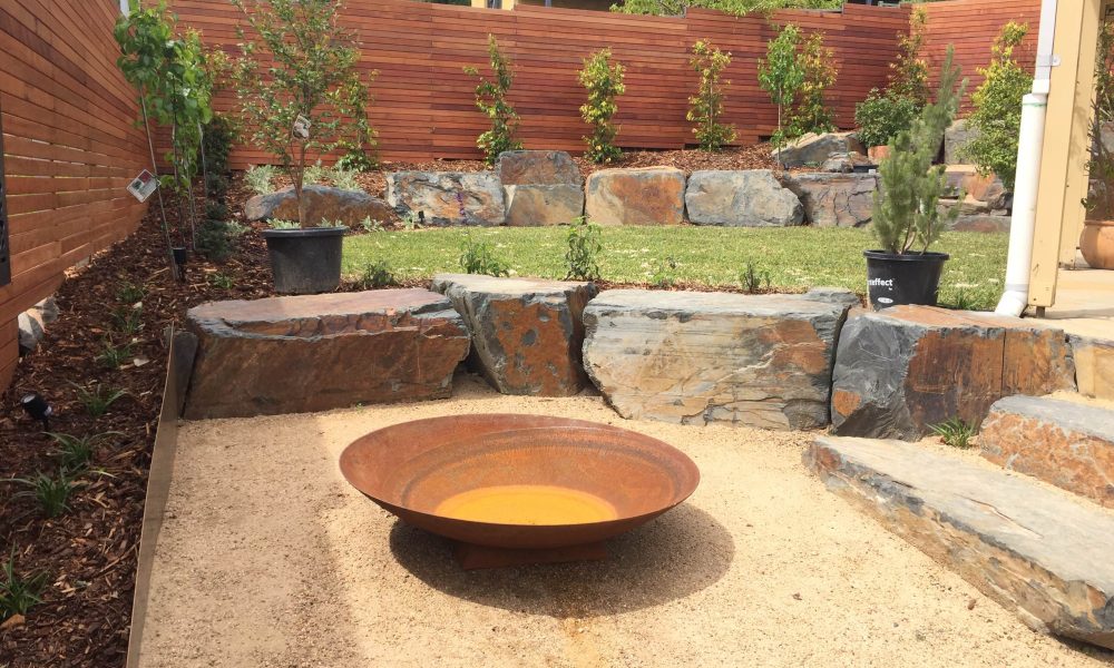 Contemporary Camberwell backyard landscaping with natural stone retaining walls, timber screening and a modern fire pit area